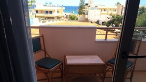 A balcony with two wicker chairs and a small table, overlooking a beach and buildings. - Artemis Bay by Estia (Hersonissos)