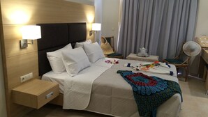 A hotel room with a bed, bedside tables, a chair, a small table with a teapot, and a curtain. - Artemis Bay by Estia (Hersonissos)