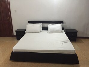 A standard hotel room with a single bed, two bedside tables, and a wooden door. - WS Diamond Hotel (Freetown)