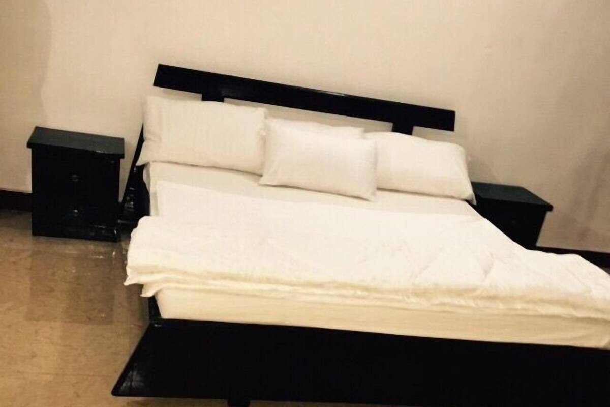 A neatly made bed with white linens and a black headboard in a room with tiled flooring.