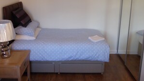 A bedroom with a bed, a nightstand, a lamp, a dresser, and a mirror.