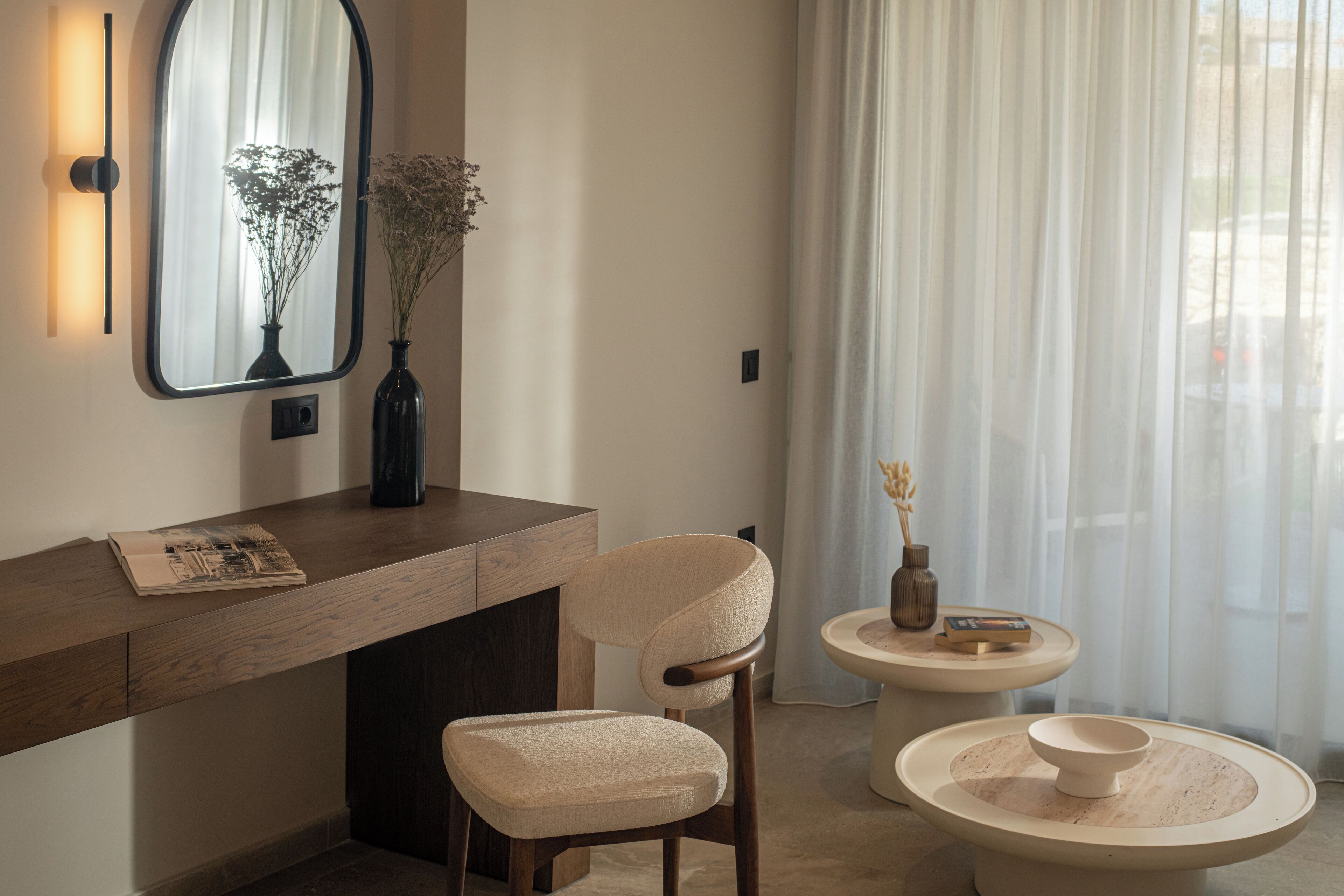 A modern room with a wooden desk, a chair, a small table with a vase, and a mirror on the wall.