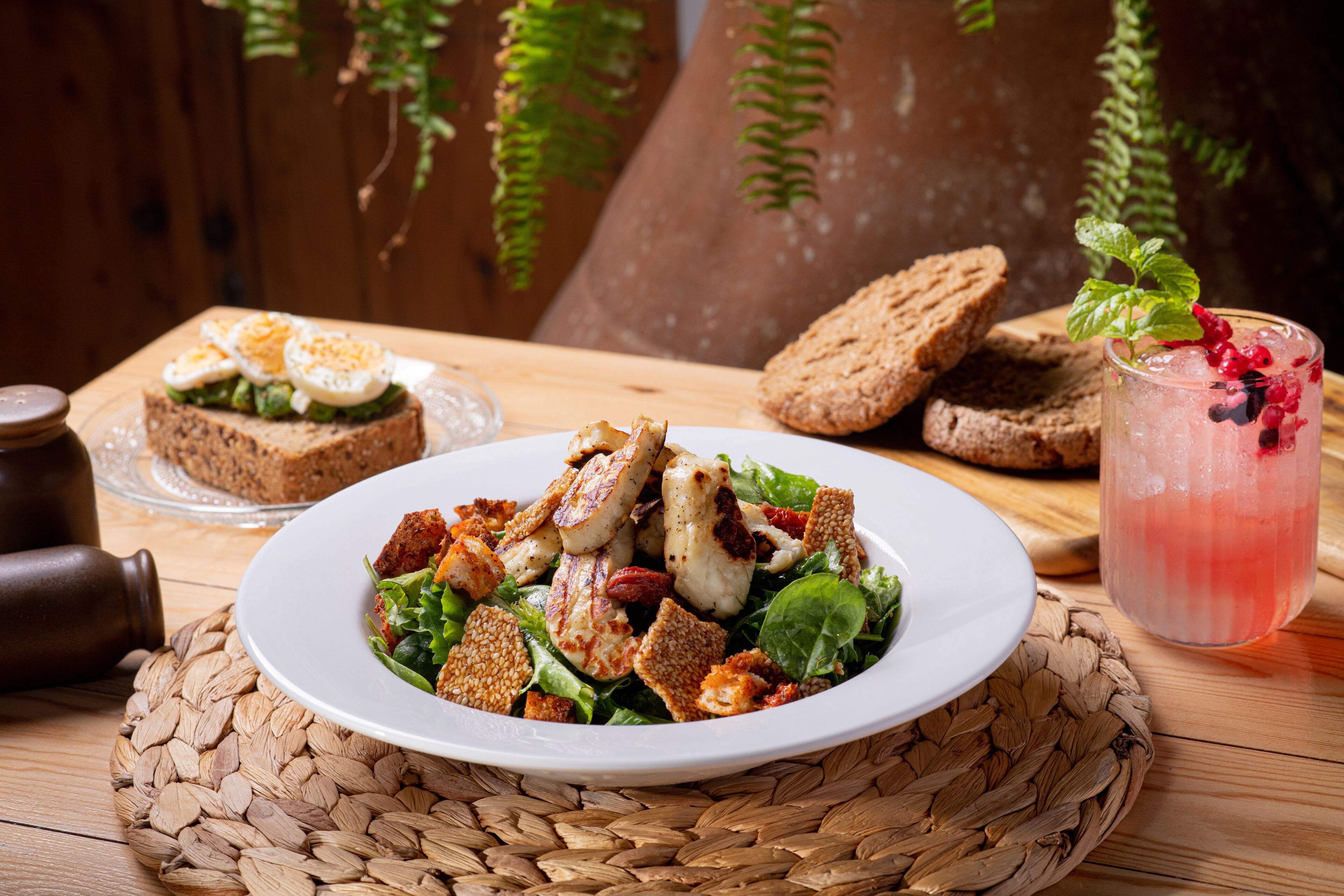 A plate of salad with croutons and a glass of iced drink with berries.