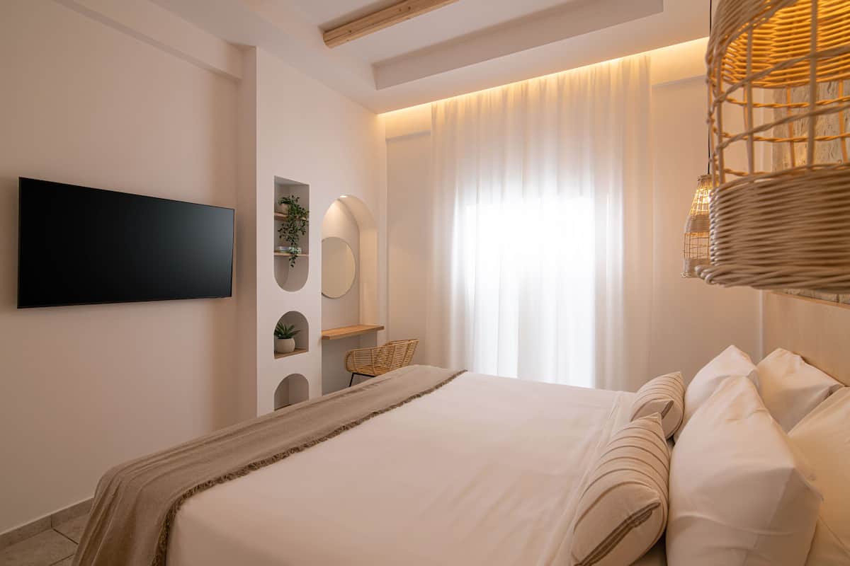 A modern bedroom with a large bed, a flat-screen TV, a wicker light fixture, and a window with sheer curtains.