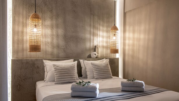 A bedroom with a large bed, two hanging light fixtures, and a textured wall.