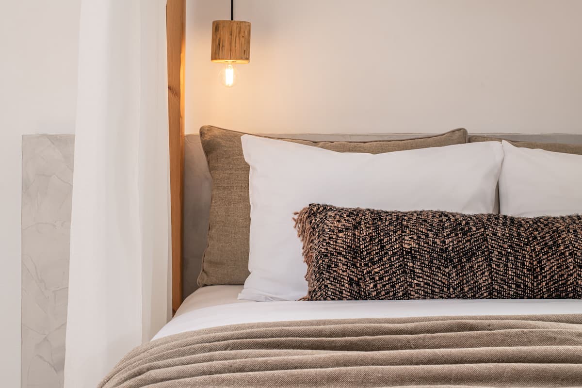 A neatly made bed with a white and brown blanket, a wooden headboard, and a hanging light fixture.