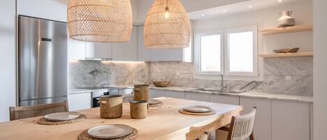 A modern kitchen with a wooden dining table, wicker pendant lights, and marble countertops.