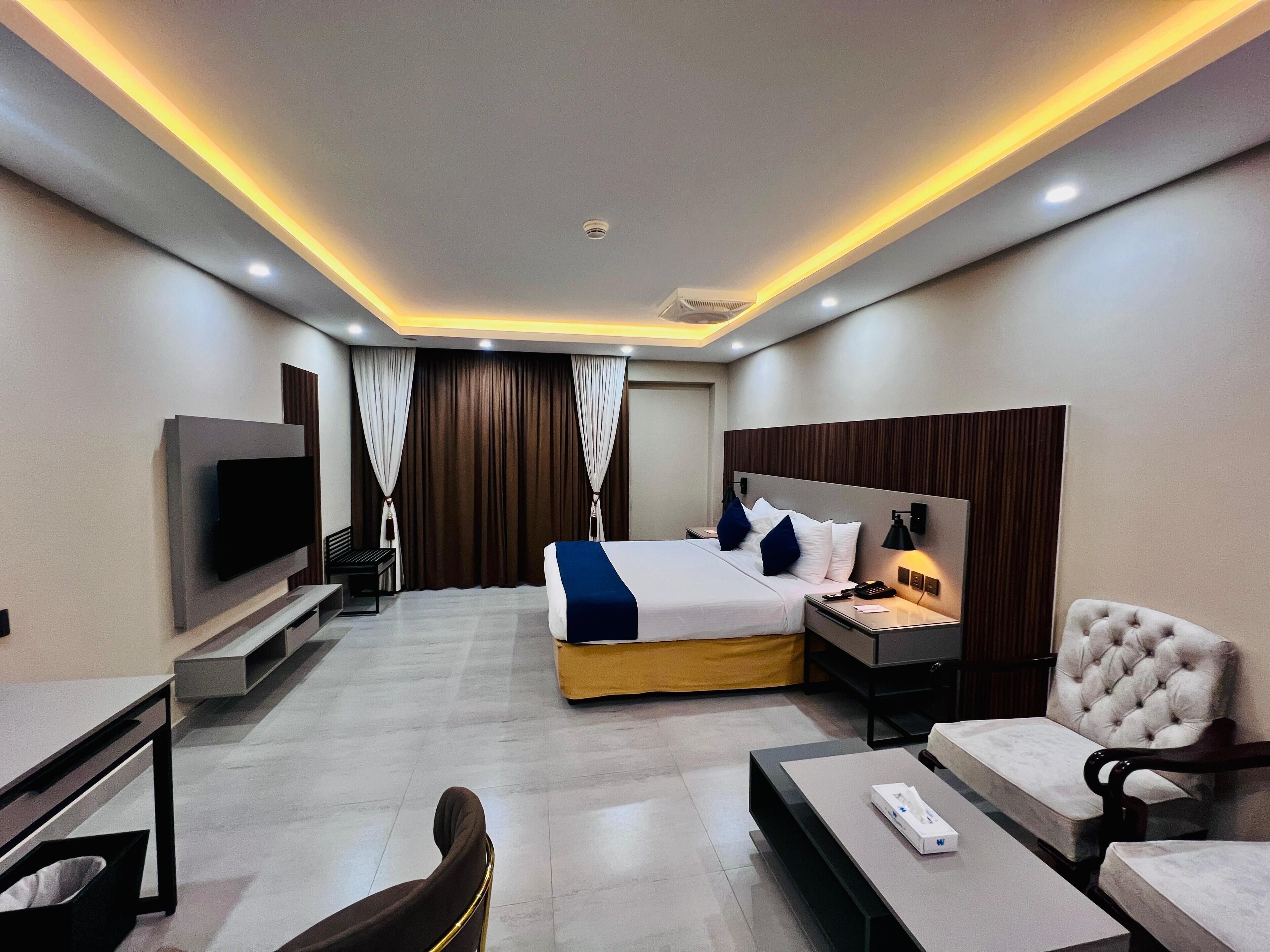 A modern hotel room with a bed, bedside tables, a TV, a desk, and a chair.