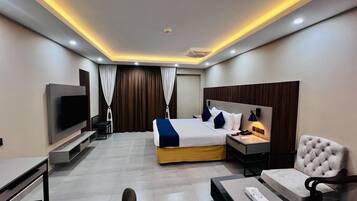 A modern hotel room with a bed, bedside tables, a TV, a desk, and a chair.