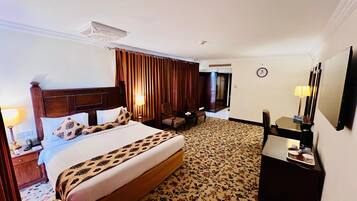A hotel room with a large bed, a desk, a chair, a mirror, and a clock on the wall.