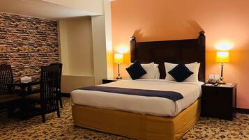 A hotel room with a large bed, two bedside tables with lamps, a dining table with chairs, and a stone accent wall.