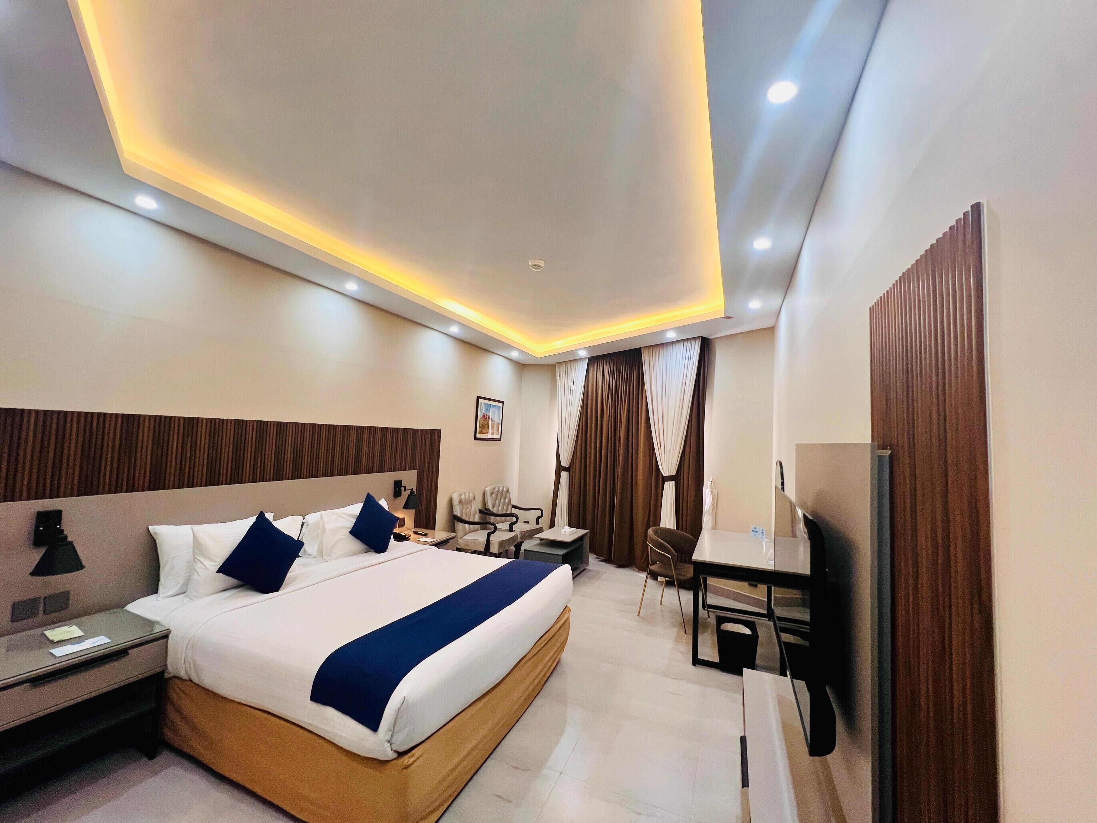 A modern hotel room with a large bed, bedside tables, a desk, a chair, and a television.