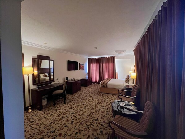 A hotel room with a bed, a desk, a chair, a television, and a large window with curtains. - Hotel Hillview Islamabad (Islamabad)
