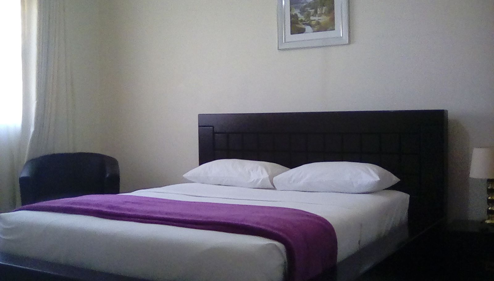 Habitació d'hotel amb un llit, una cadira i una tauleta de nit amb una làmpada.
