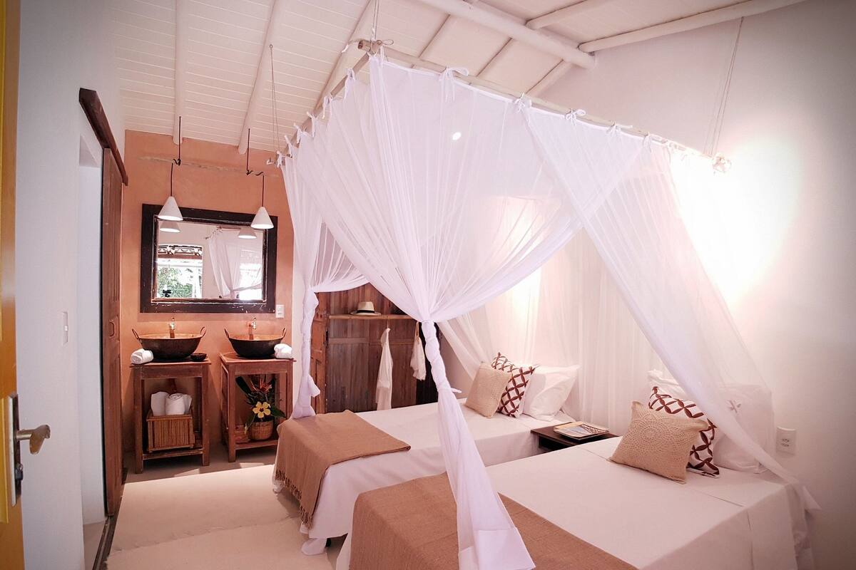A bedroom with a canopy bed, a wooden vanity, a mirror, and a window.