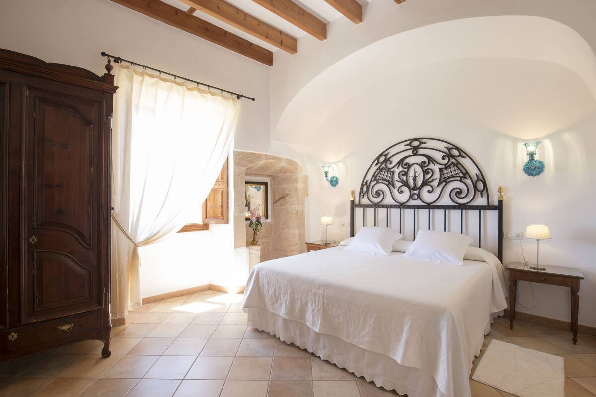 A bedroom with a large bed, a wooden wardrobe, a stone wall, and a decorative metal headboard.