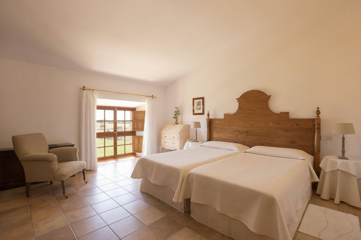 A bedroom with two beds, a chair, a nightstand, and a window with curtains.