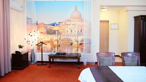 A hotel room with a large window featuring a scenic view of a bridge and a historic building. There is a bed, a desk, two chairs, and an air conditioning unit. - Hotel San Marino (Astana)