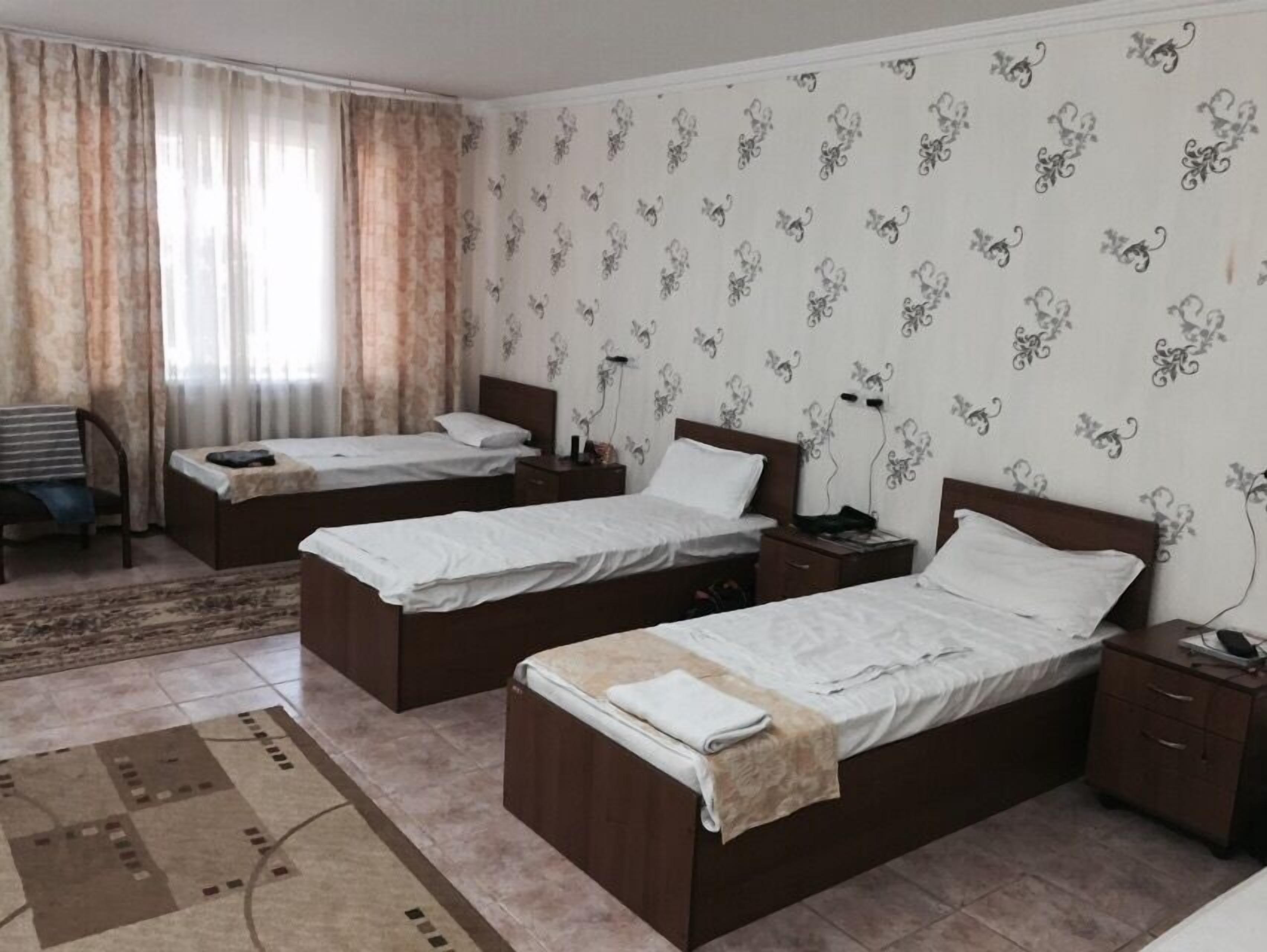 A hotel room with two single beds, a small desk, a chair, and a patterned wall.