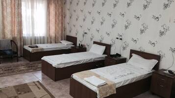 A hotel room with two single beds, a small desk, a chair, and a patterned wall.
