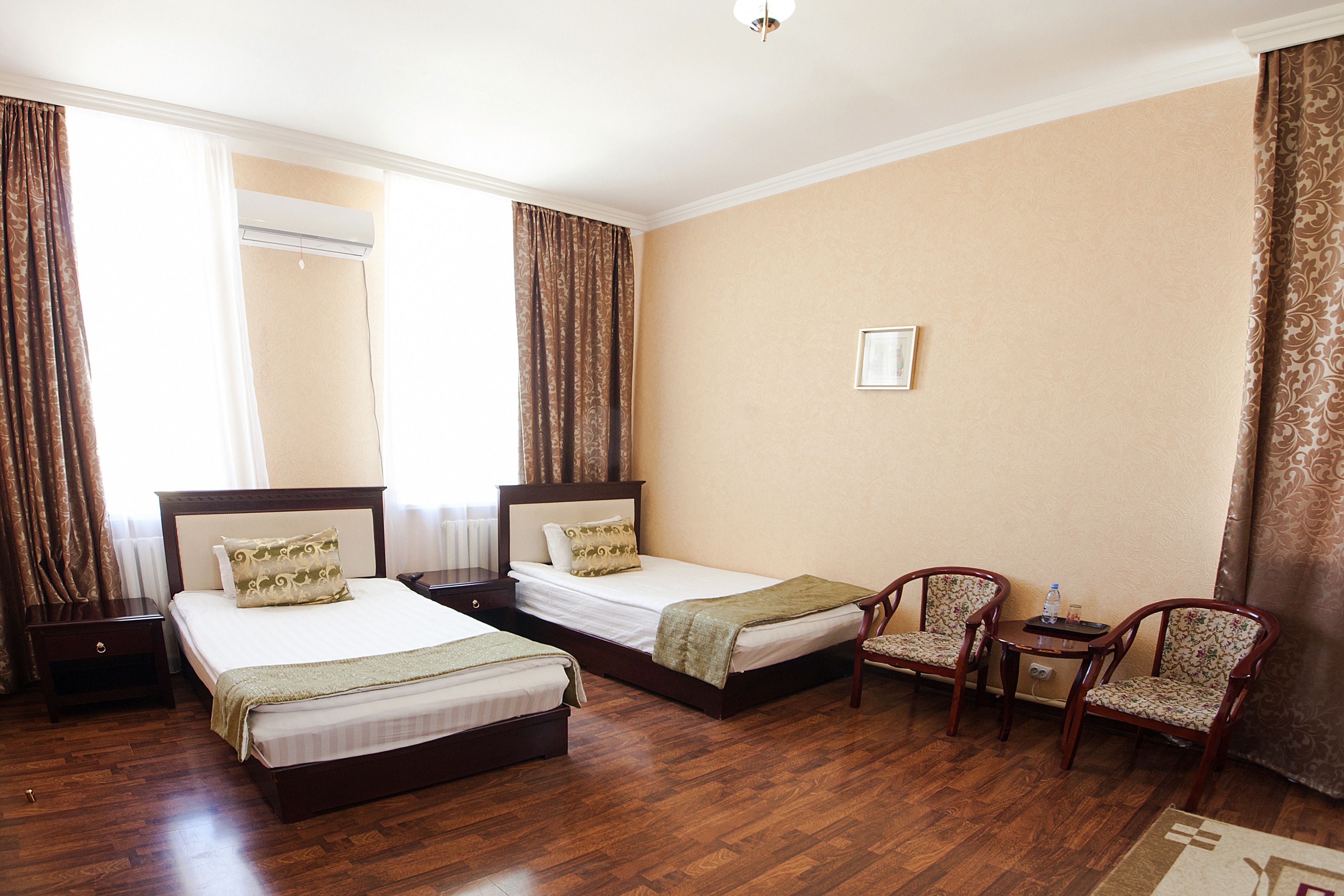 Habitación de hotel con dos camas, una mesita, dos sillas y un ventanal con cortinas.