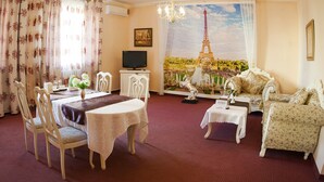 A living room with a dining area, a sofa, a TV, and a large window with a view of the Eiffel Tower. - Hotel San Marino (Astana)