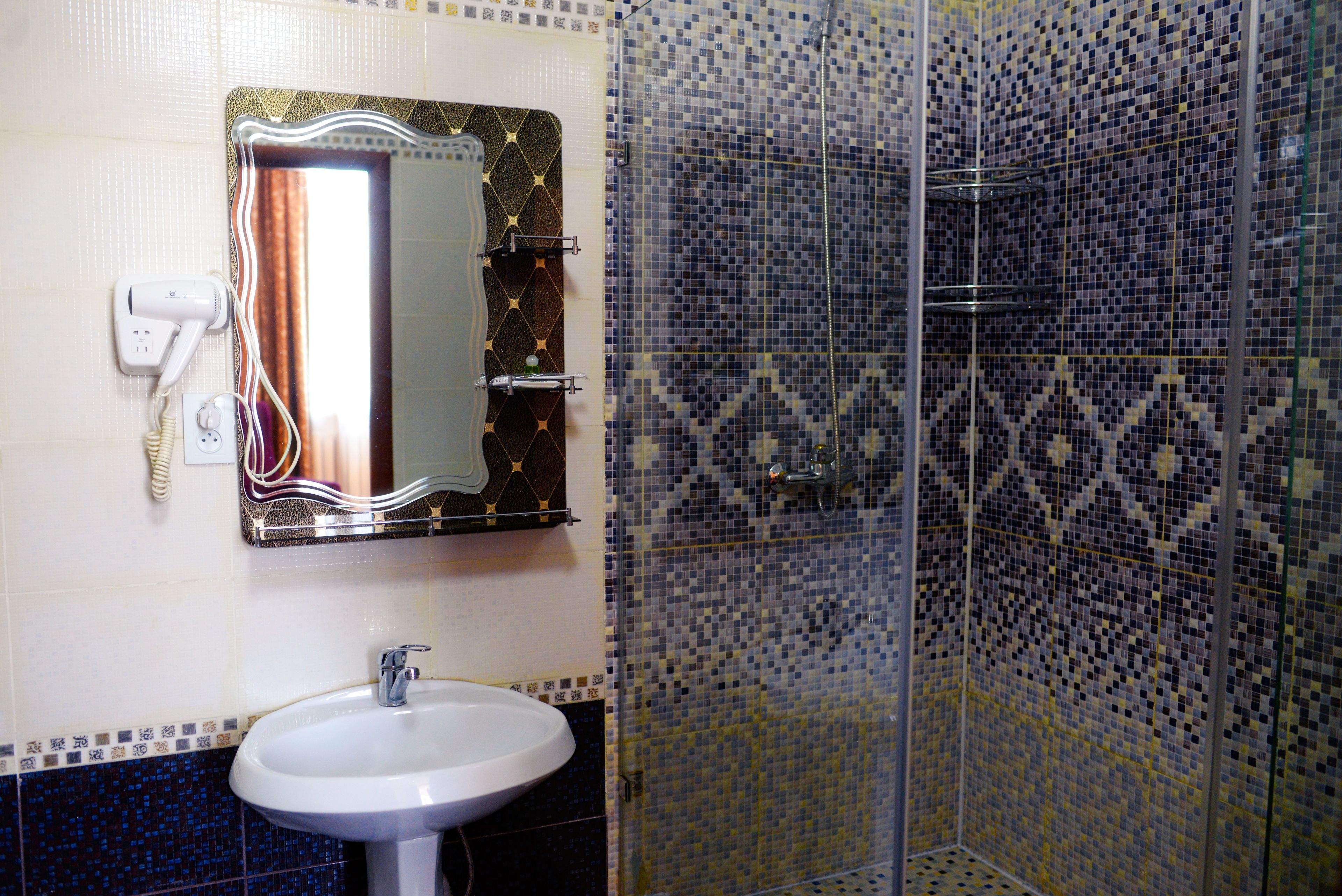 A bathroom with a white sink, a mirror with a gold frame, and a shower with mosaic tiles.