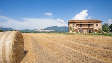 Un paisaje rural con un gran fardo de heno y un edificio de dos pisos con tejado de tejas.