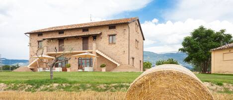 A rustic house with a brick exterior, a balcony, and a large hay bale in the foreground.