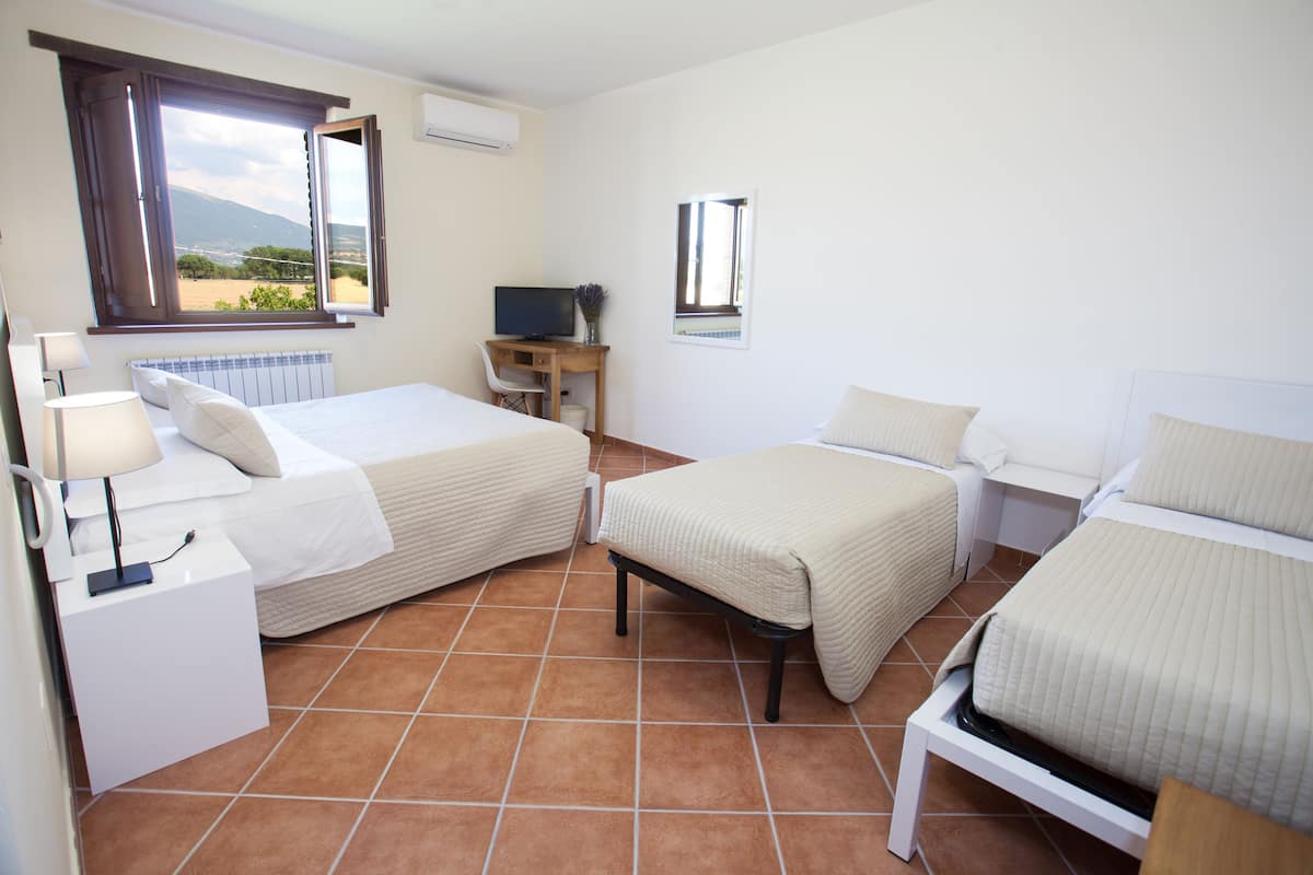 A hotel room with two beds, a desk with a TV, a chair, and a window with a view of the outdoors.
