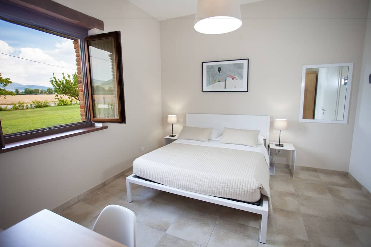 A bedroom with a bed, bedside tables, a window with a view of a garden, and a framed picture on the wall.