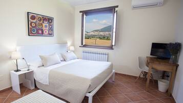 Um quarto com cama, escrivaninha, cadeira, televisão e janela com vista para a paisagem.
