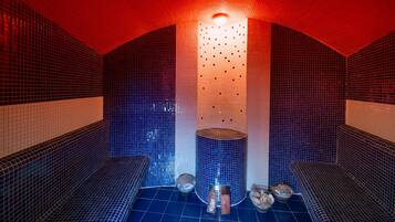 Uma sauna com paredes e bancos revestidos em azulejos, um pilar central e um acessório de iluminação.