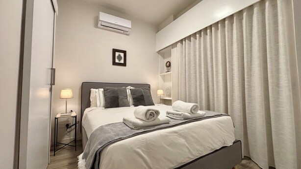Una cama bien hecha con toallas enrolladas, una lámpara de noche y una mesita con lámpara.