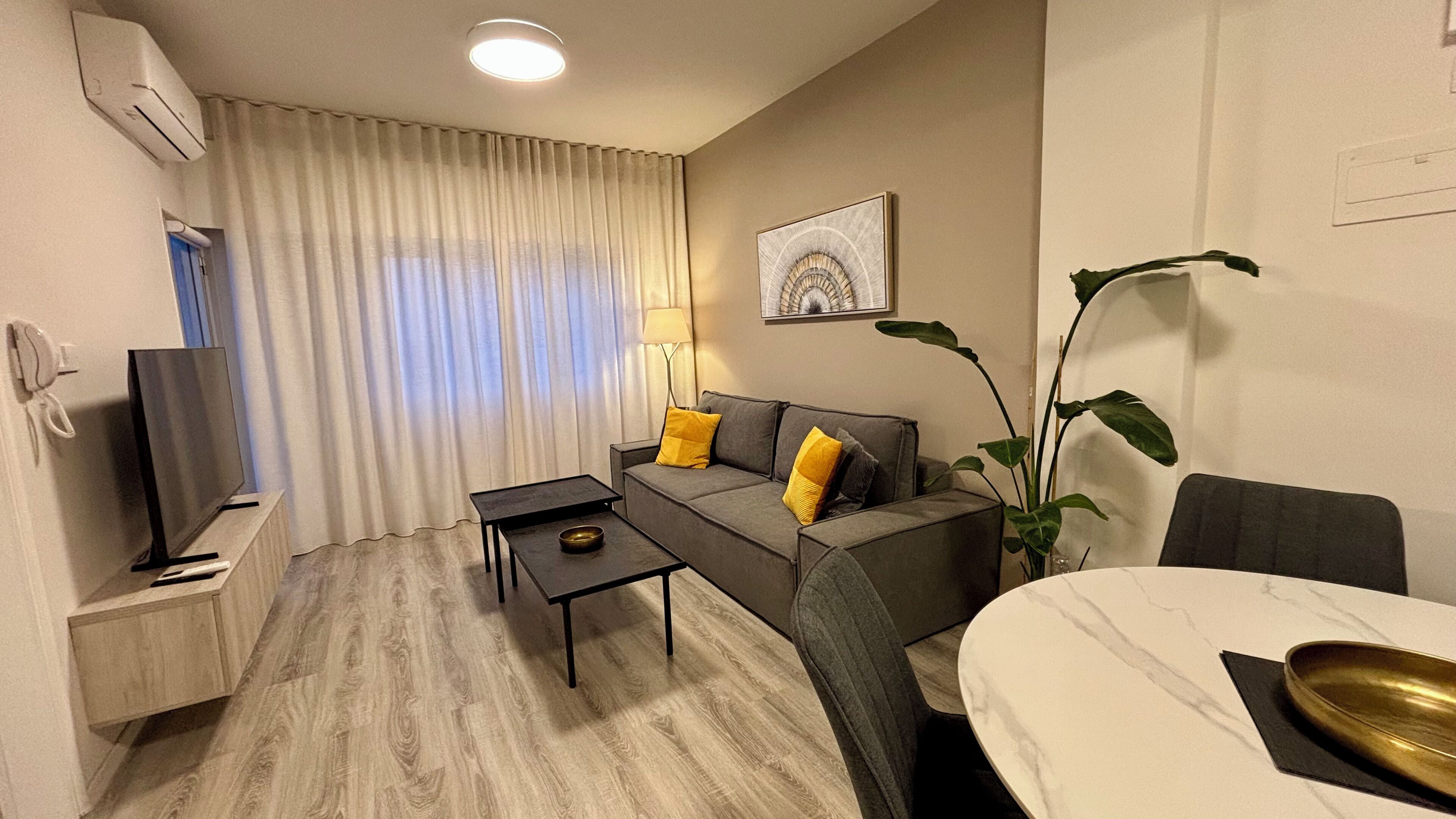 A compact living space with a sofa, a small table, a TV, a lamp, and a dining table.
