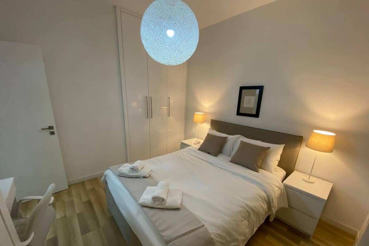 A neatly arranged hotel room with a bed, two bedside tables with lamps, a wardrobe, and a chair.