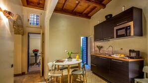 A compact kitchen with dark cabinetry, a built-in microwave, and a coffee machine. There is a small dining area with a round table and chairs. - Palazzo Medusa (Rome)