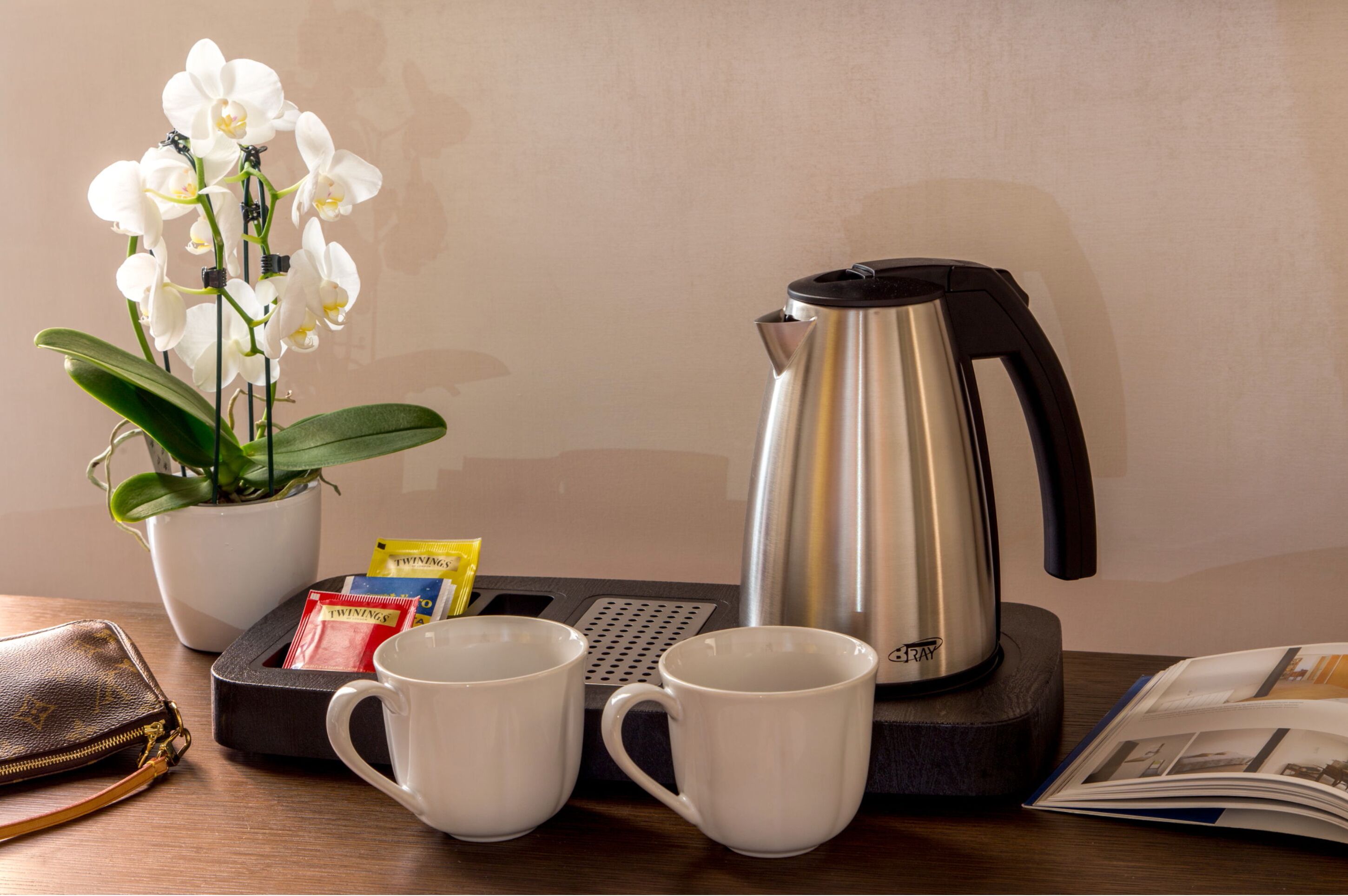 Ein Tisch mit Kaffeemaschine, zwei weißen Tassen, einem Topf mit Orchideen, einer Brieftasche und einer Zeitschrift.