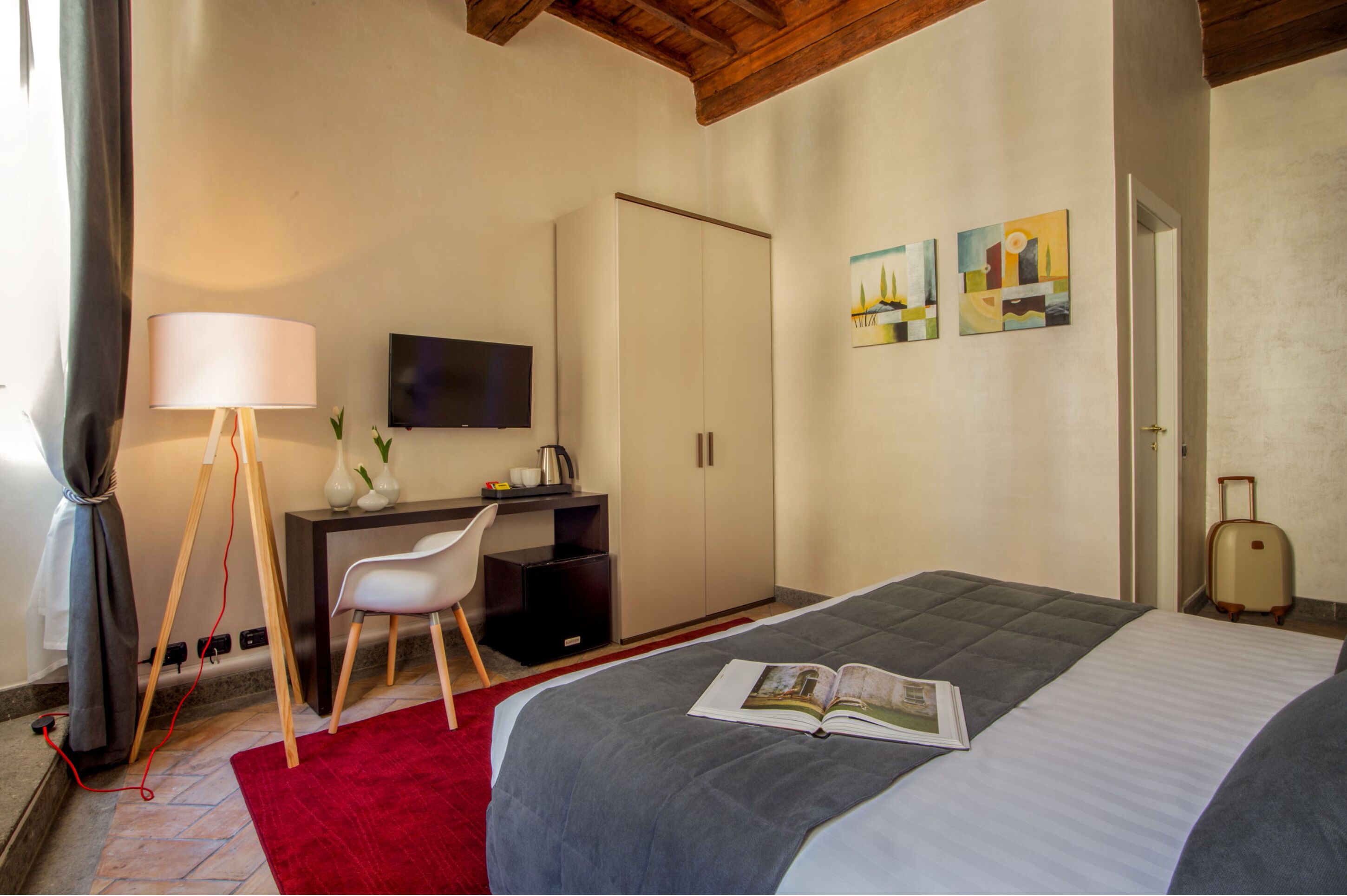 A hotel room with a bed, a desk with a chair, a television, and artwork on the wall.