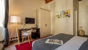 A hotel room with a bed, a desk with a chair, a television, and artwork on the wall.
