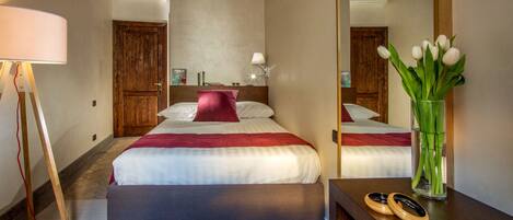A hotel room with a bed, a mirror, a nightstand, a lamp, and a vase with flowers.