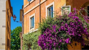 A building with a balcony covered in purple flowers, a statue, and a sign that reads "Caffetteria." - Palazzo Medusa (Rome)