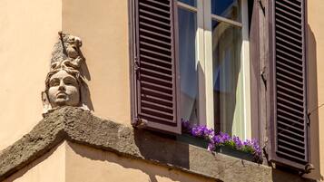 Un coin d’immeuble orné d’une sculpture en pierre, une fenêtre avec des volets et des fleurs violettes dans une jardinière.