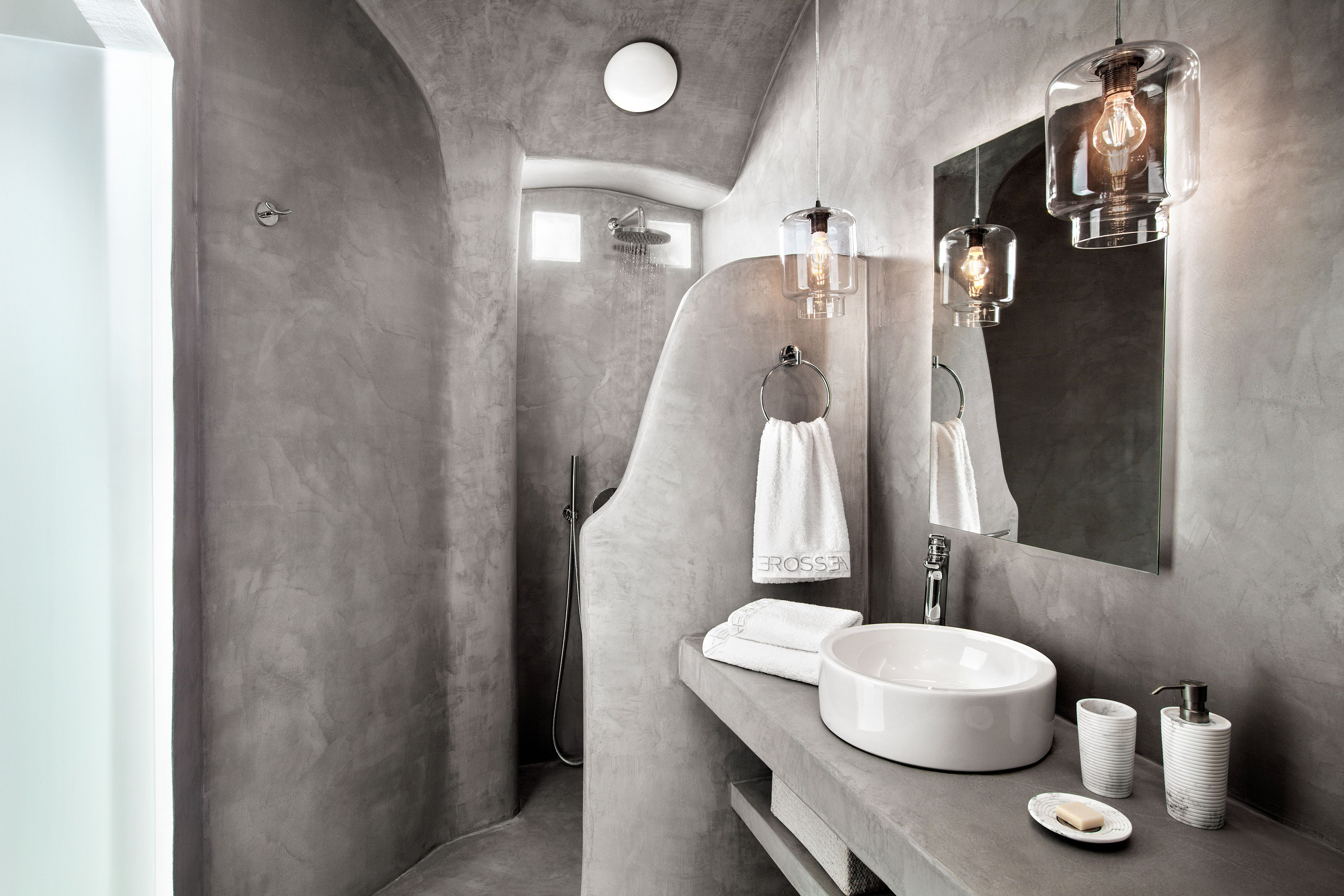 A modern bathroom with a curved shower, a round mirror, and a white sink with a soap dish.