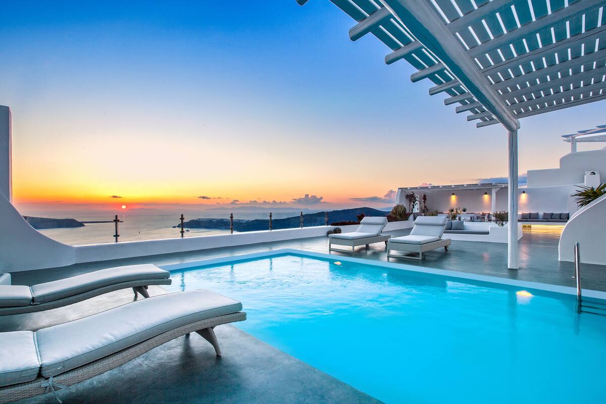 Ein moderner Infinity-Pool mit weißen Liegestühlen und Blick auf den Sonnenuntergang über dem Meer.