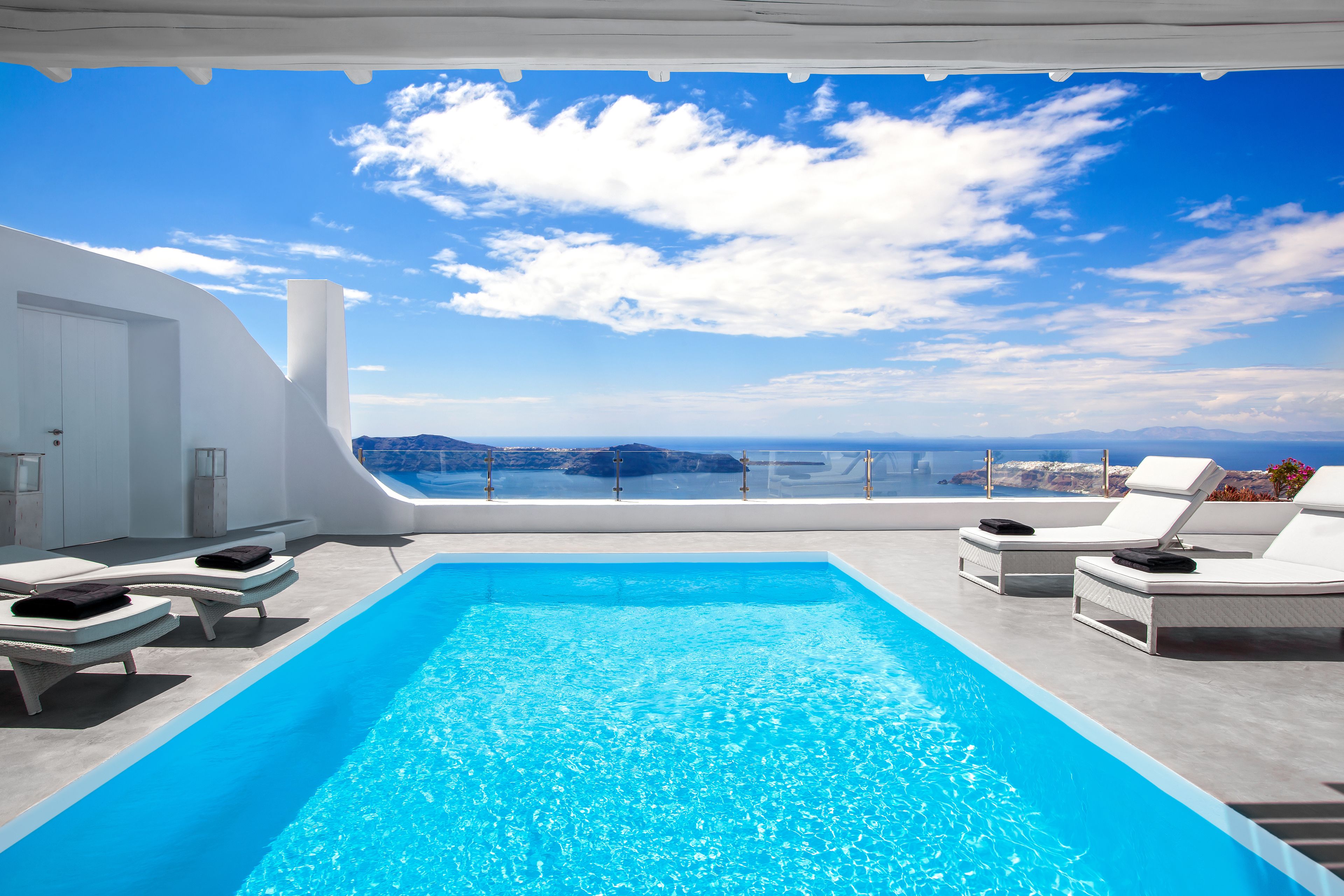 A pool area with lounge chairs and a view of the sea.