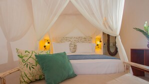 Een bed met hemelbed, twee kussens, een bedlampje en een wandlamp.