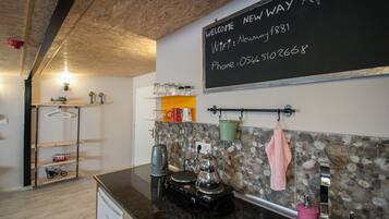 A kitchen with a blackboard displaying a welcome message, a coffee machine, a kettle, and a sink.