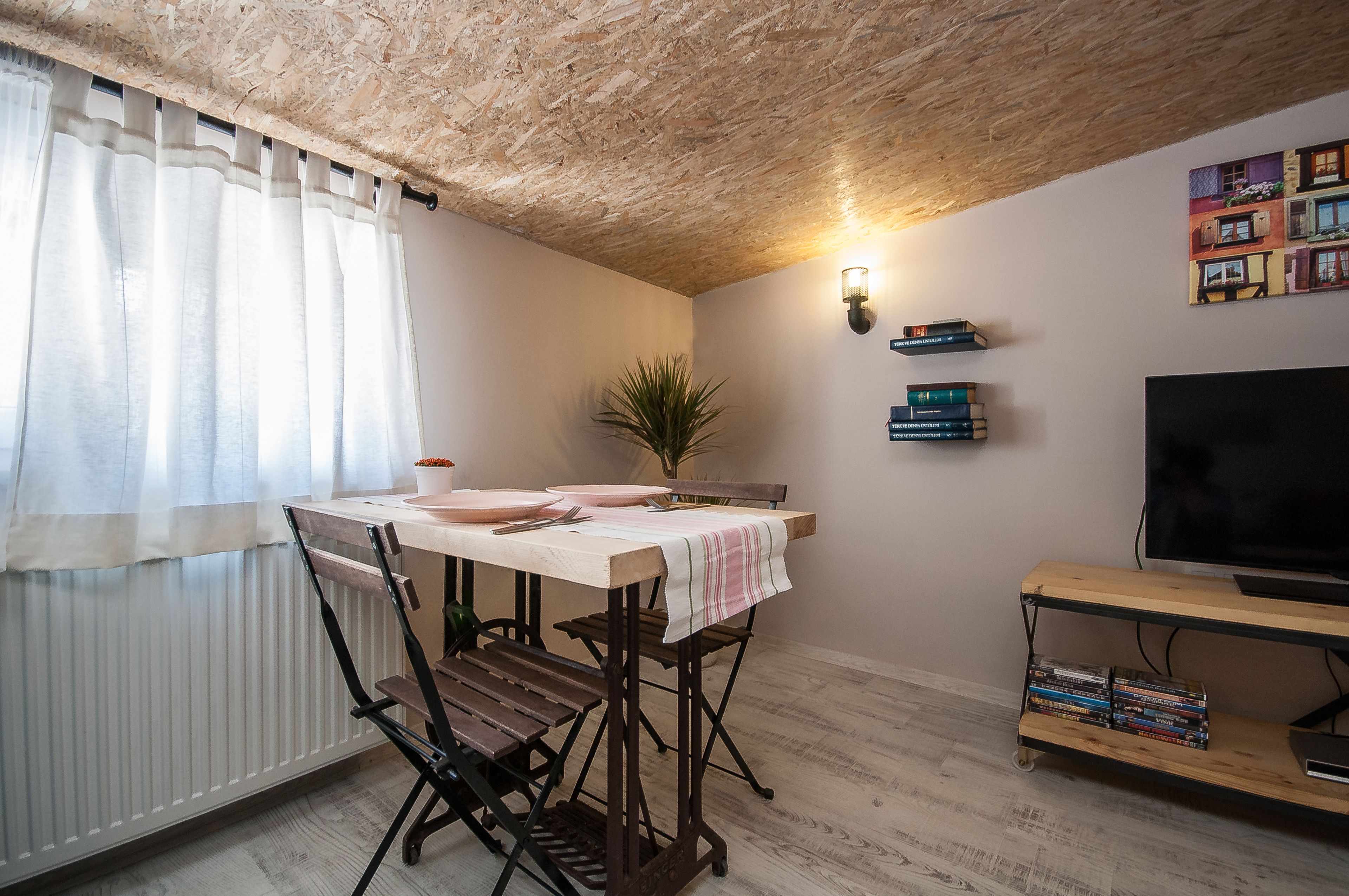 Een eetgedeelte met een tafel voor twee personen, een bloempot en een boekenkast met boeken.