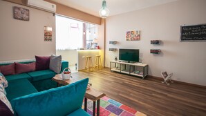 Una sala de estar moderna con un sofá azul turquesa, una mesa de centro de madera, un televisor sobre un mueble bajo y una alfombra colorida.